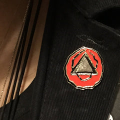 Dripper World Sacred Bones Logo Enamel Pin featuring red and silver geometric design on black fabric lapel.
