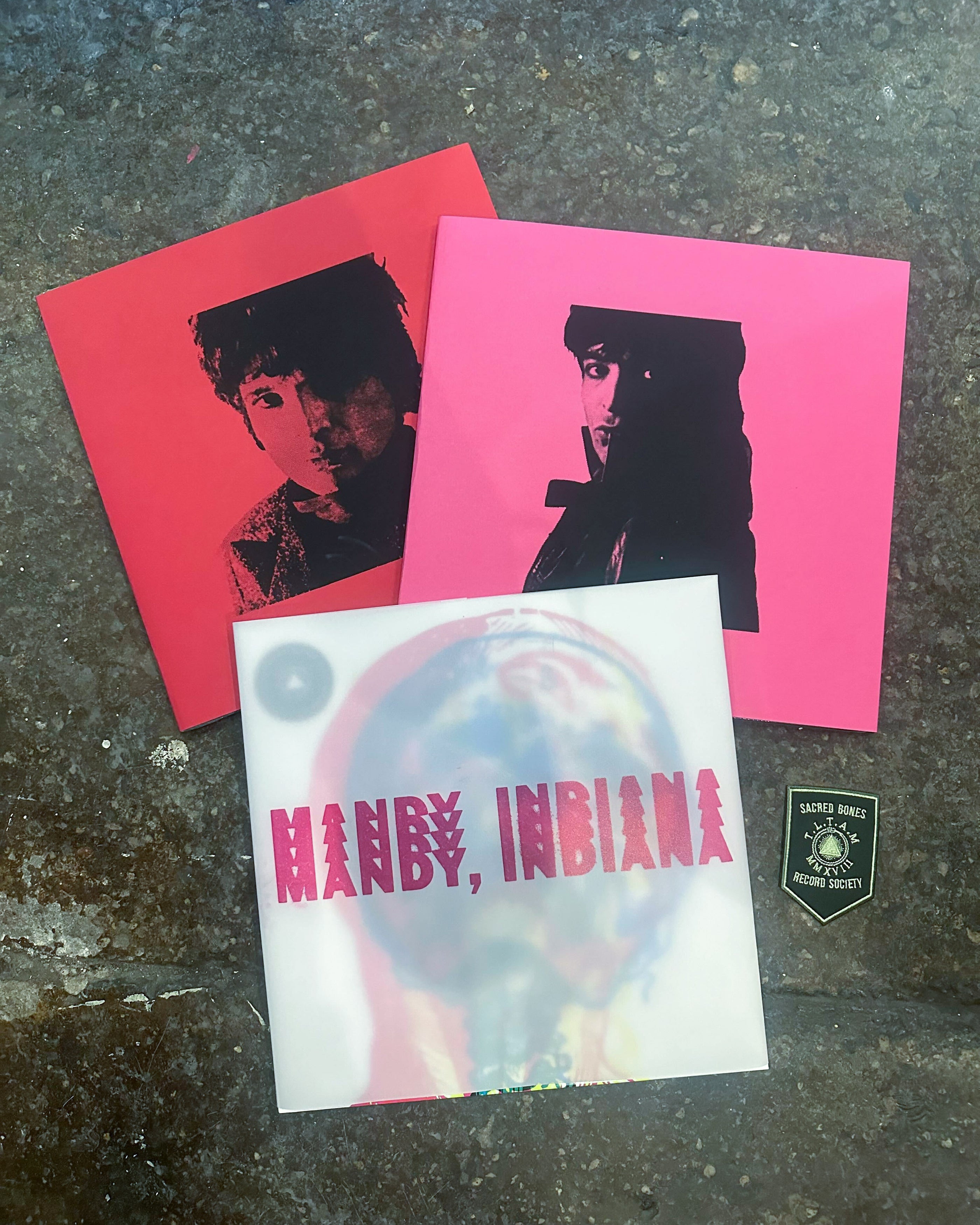 Immigration Solidarity Record Raffle featuring vinyl records with red and pink covers and a Sacred Bones patch