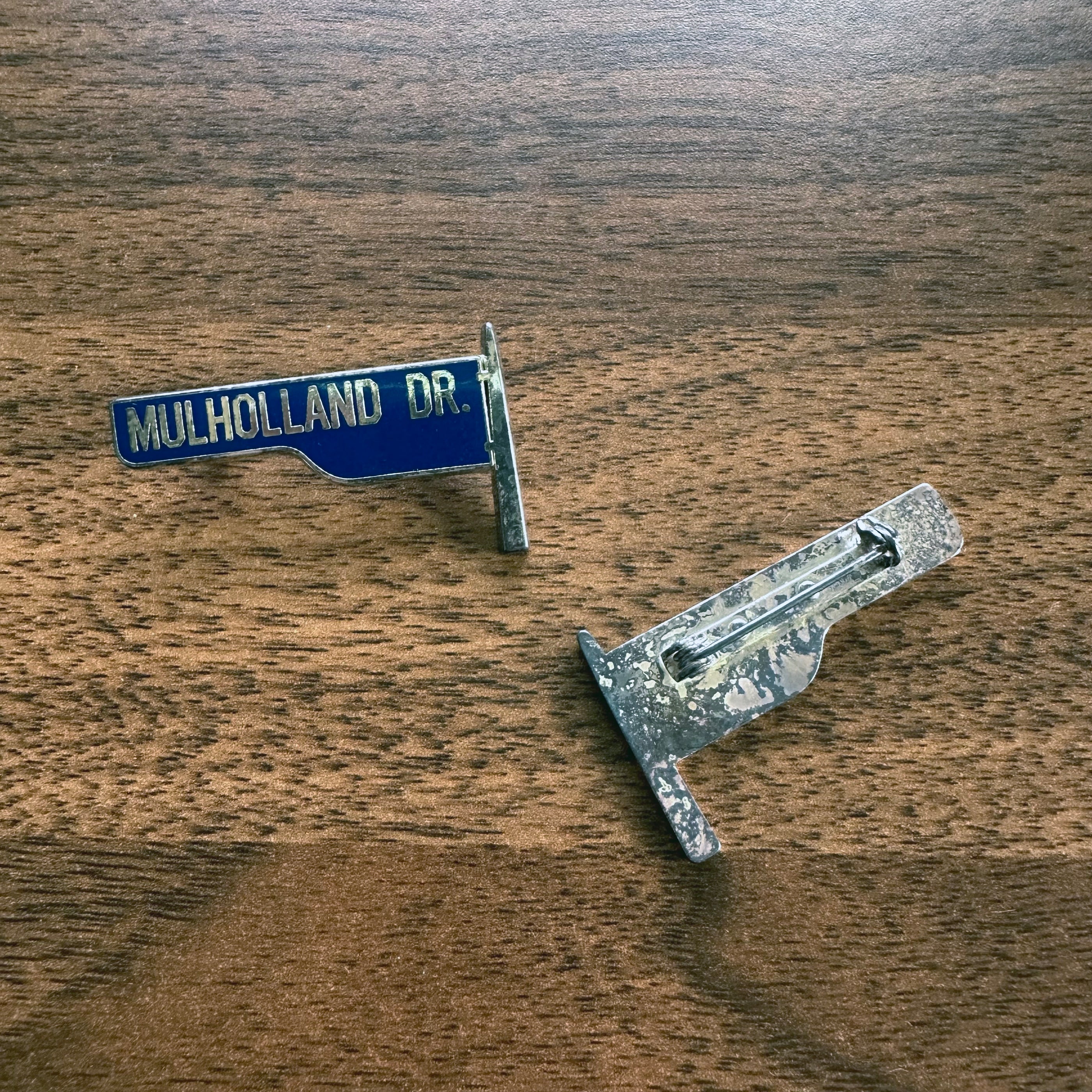 Mulholland Drive Pin enamel street sign design with blue background and silver backing on wooden surface